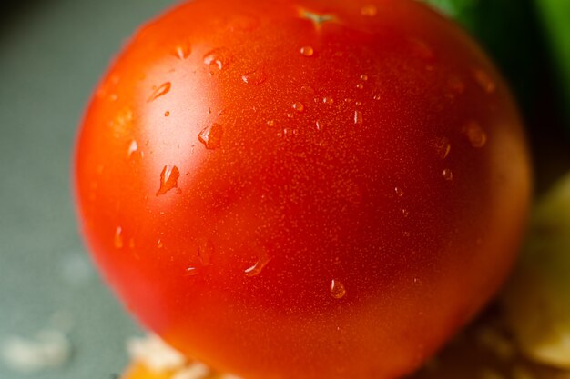 Foto met focus op gewassen rode tomaat ligt op de tafel met druppels water erop