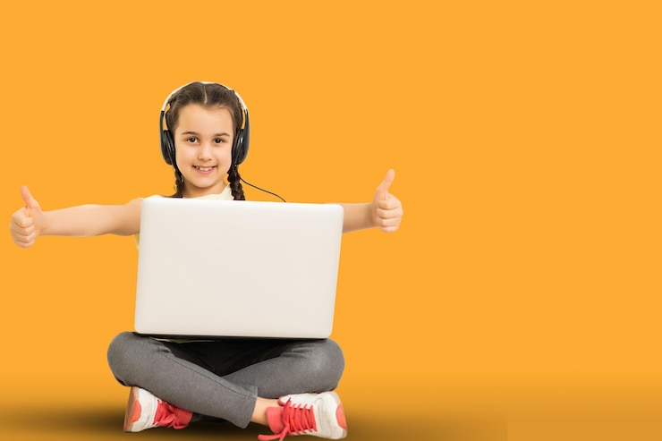 Foto over de volledige lengte van een positief geïnteresseerd kind zit met gekruiste benen gevouwen, werkt op haar laptop, leest nieuws op sociale media en draagt casual kleding geïsoleerd op een gele achtergrond.