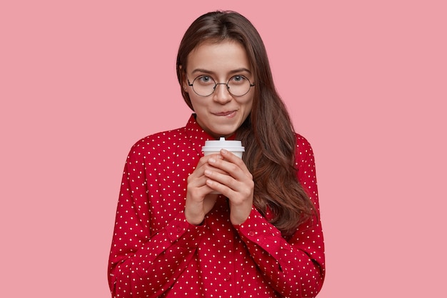 Foto van aantrekkelijke dame met donker haar, bijt onderlip, kijkt met tevreden verlegen uitdrukking, gekleed in formeel overhemd