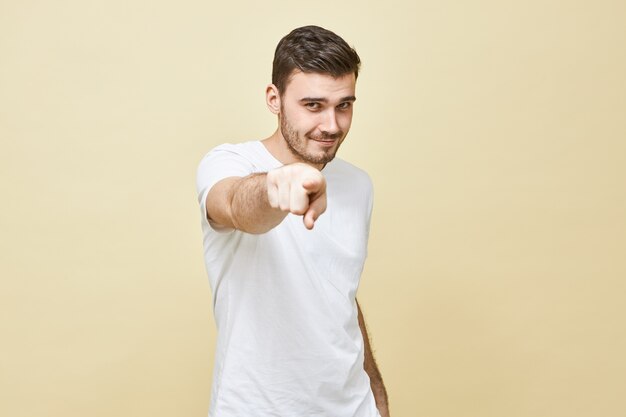 Foto van aantrekkelijke zelfverzekerde jonge brunette man in wit casual t-shirt op zoek recht en wijsvinger, waardoor je vertrouwen hebt, briljant idee. Selectieve aandacht