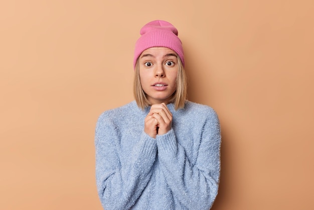 Foto van bezorgde geschrokken jonge vrouw houdt handen bij elkaar staat sprakeloos hoort groot nieuws kan eigen ogen niet geloven gekleed in vrijetijdskleding geïsoleerd over bruine achtergrond. Menselijke reacties.