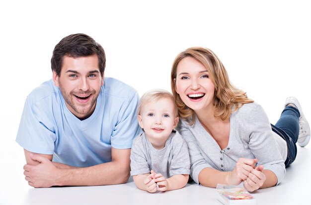 Foto van de glimlachende jonge ouders met klein kind dat op de geïsoleerde vloer ligt -