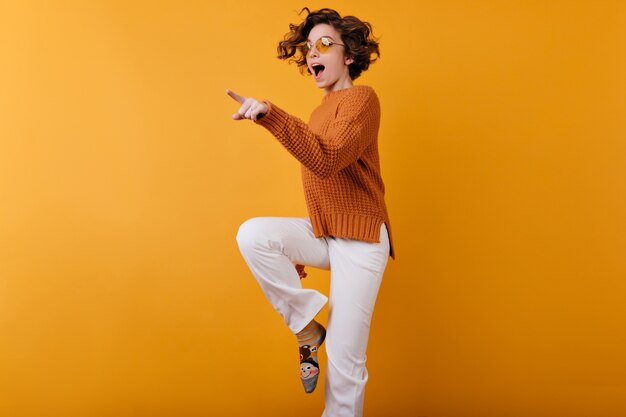 Foto van donkerharige meisje in wollen trui dansen op oranje ruimte met glimlach