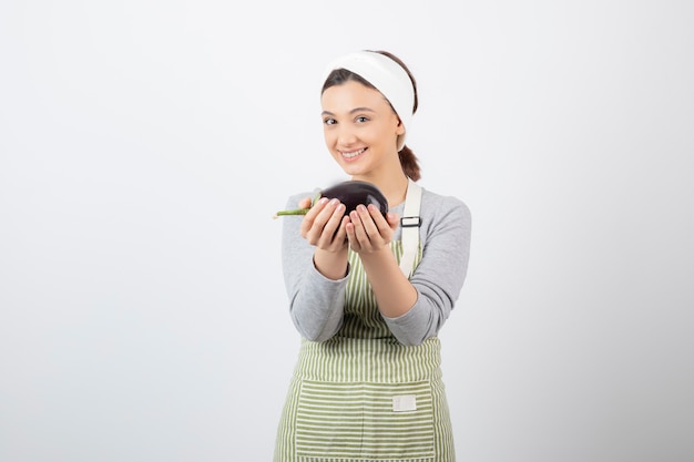 Foto van een aardig jong vrouwenmodel in schort met een aubergine