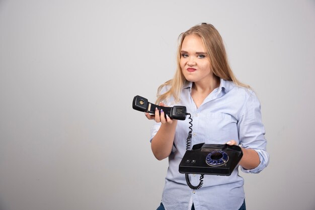 Foto van een boos vrouwenmodel dat staat en een zwarte oude handset vasthoudt