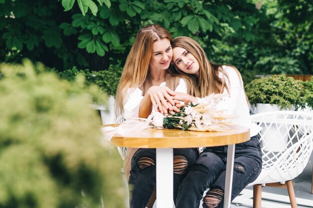 Foto van een gelukkig meisje dat op de schouder van haar moeder ligt en naar de camera kijkt