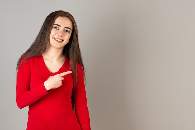 Foto van een glimlachend schattig meisje in een rood sweatshirt dat op een grijze muur staat.