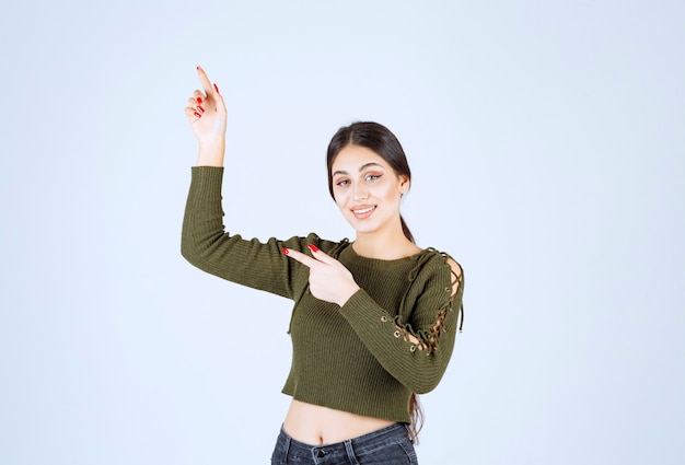 Foto van een jong glimlachend vrouwenmodel dat staat en opzij wijst met wijsvingers