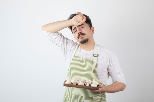 Foto van een jonge mannelijke kok die rauwe champignons vasthoudt en moe wordt