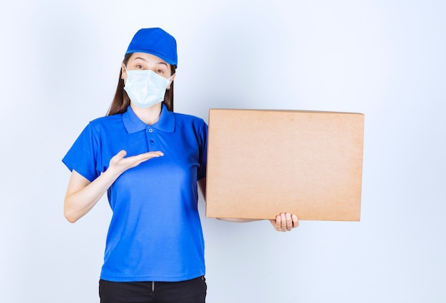 Foto van een jonge vrouw in uniform en medisch masker met papieren doos.