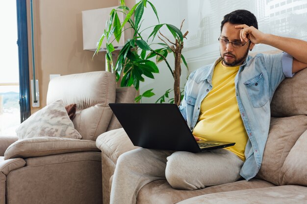 Foto van een knappe Spaanse man zittend op een bank en met behulp van een laptop