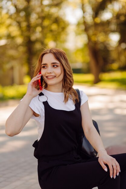 Foto van een positieve vrolijke tienermeisje brengt tijd door in het park en het gebruik van mobiele telefoon.