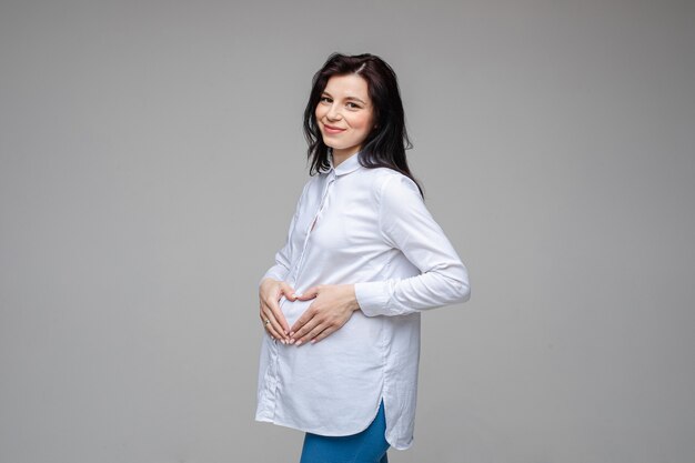 Foto van een vrolijke blanke vrouw met zwart haar en mooie glimlach in wit overhemd en spijkerbroek poseren voor de camera