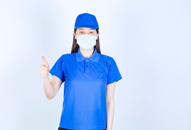 Foto van een vrouw in uniform en medisch masker die duim toont.