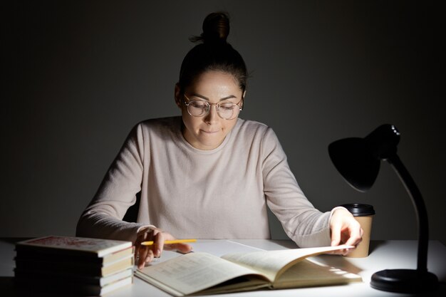 Foto van gefocuste vrouw heeft haarknoop, heeft ernstige slimme uitdrukking in leerboek