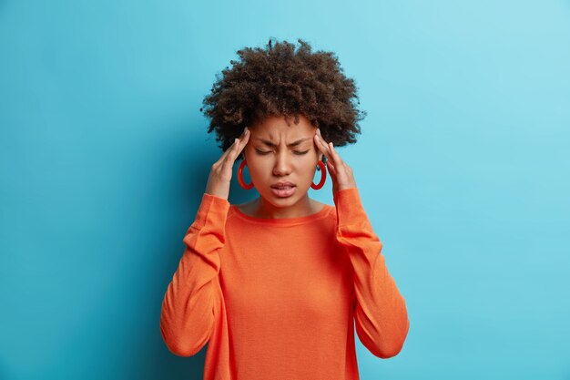 Foto van gefrustreerde jonge Afro-Amerikaanse vrouw heeft hoofdpijn houdt handen op tempels lijdt aan ondraaglijke migraine