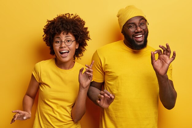 Foto van gelukkige Afrikaanse paar dansen samen tegen gele achtergrond, lichaam actief bewegen