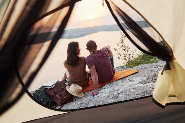 Foto van gelukkige paar zitten in tent met uitzicht op meer tijdens wandeltocht.