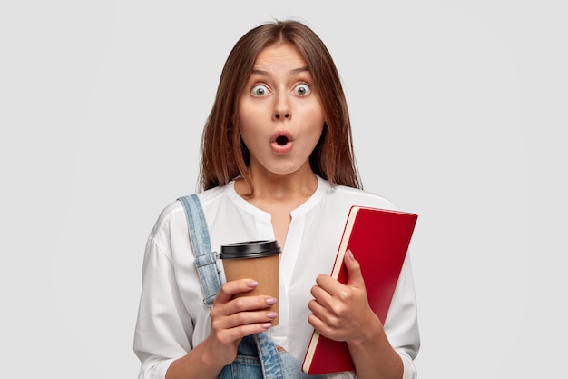 Foto van geschokt vrouw met kopje koffie en notebook in handen