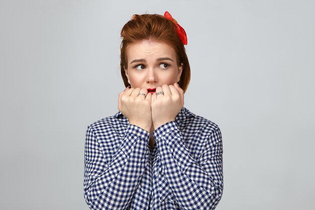 Foto van geschokte aantrekkelijke stijlvolle jonge blanke vrouw met vingerhaar wegkijken met een bange uitdrukking, hand in hand naar haar gezicht, bang van plotseling angstaanjagend geluid, alleen thuis zijn