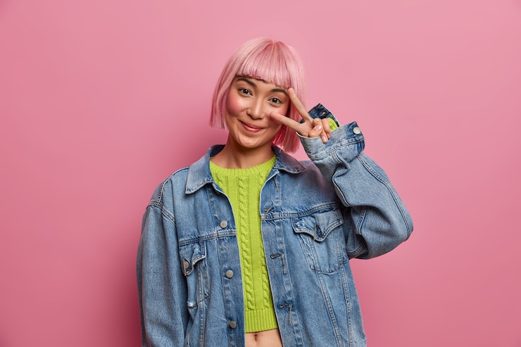Gratis Foto foto van jonge verleidelijke vrouw met trendy roze kapsel, toont victroy gebaar over oog, stijlvolle denim jasje draagt, heeft plezier, poses