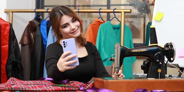 Foto van jonge vrouwelijke kleermaker die selfie neemt in het atelier