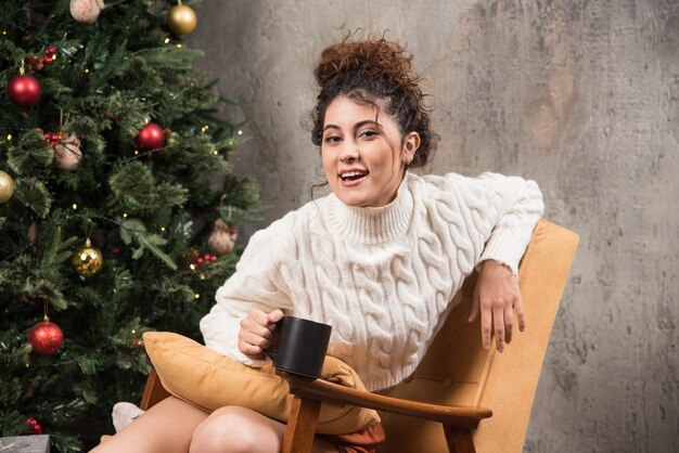 Foto van lachende vrouw zittend in een comfortabele stoel met een kopje drank