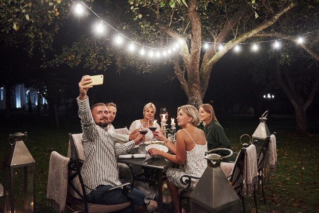 Foto van man neemt selfie. Groep vrienden in de elegante kleding hebben een luxe diner