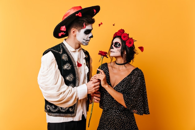 Foto van paar in liefde met roos. Man en vrouw met gezichtskunst kijken elkaar zachtjes in de ogen.