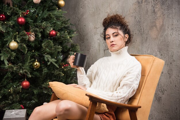 Foto van peinzende vrouw zittend in een comfortabele stoel met een kopje drank