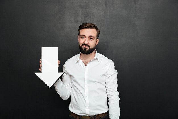 Foto van pessimistische overstuur man 30s met lege toespraak pijl wijzer naar beneden gericht over donkere grijze muur kopie ruimte