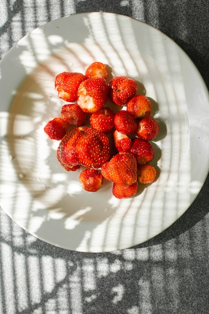 Gratis foto foto van sappige verse rijpe rode aardbeien in een witte keramische plaat op tafel onder fel zonlicht in een dorp