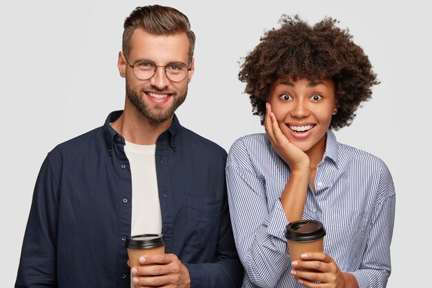 Foto van tevreden gemengd ras vrouw en man houdt wegwerp kopje koffie