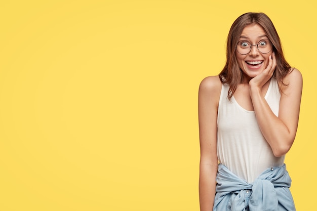 Foto van tevreden jonge blanke vrouw glimlacht positief, houdt hand op kin, in goed humeur