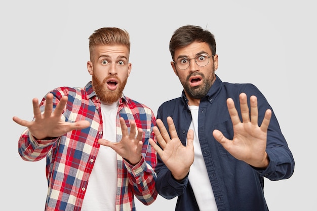 Foto van twee mannen hebben angstige uitdrukkingen, maken een bang gebaar met de handpalmen, proberen zich te verdedigen tegen iets slechts