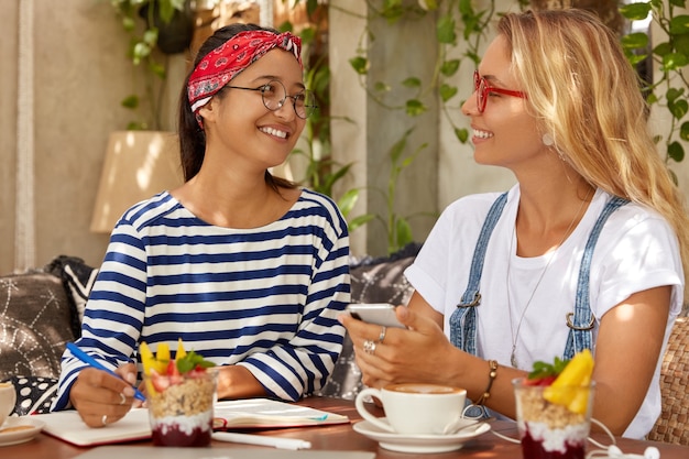 Foto van twee vriendelijke vrouwen schrijven gelukkige momenten over hun vakantie op een exotische plek in notitieboekje