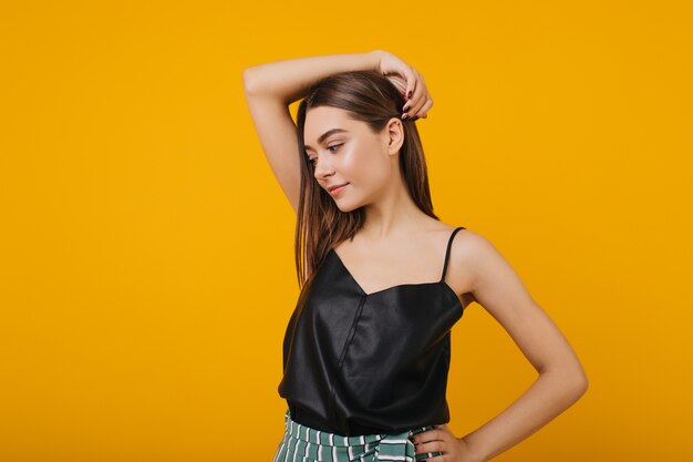 Foto van verfijnd bruinharig geïsoleerd meisje. Portret van het overweldigen van ernstige blanke vrouw poseren in zwarte tank-top.