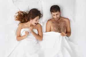Gratis foto foto van volwassen europese bebaarde man en opgewonden vrouw in bed liggen en gluren onder een witte deken