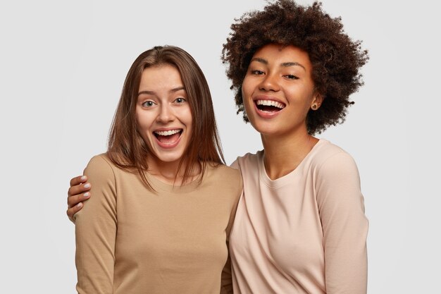 Foto van vrolijke dames omarmen en genieten van saamhorigheid, van verschillende rassen, gekleed in casual truien