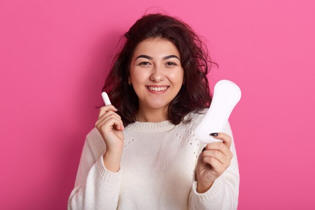 Foto van vrolijke energieke vrouw met donker krullend haar, staande geïsoleerd over roze