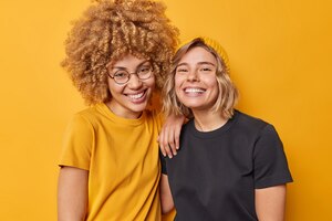 Foto van vrolijke jonge mooie vrouwen staan naast elkaar gekleed in casual t-shirts glimlach gelukkig geïsoleerd over levendige gele studio achtergrond mensen vriendschap positieve emoties concept