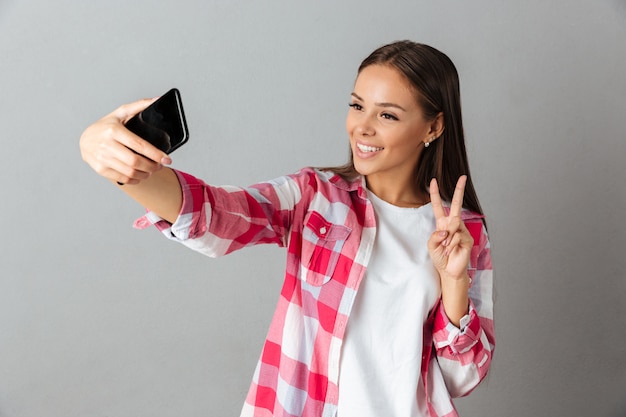 Foto van vrolijke jonge vrouw in geruit hemd, selfie te nemen door haar telefoons