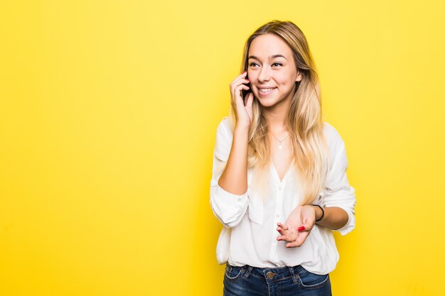 Foto van vrolijke leuke mooie jonge vrouwenbespreking op mobiele telefoon die over gele muurmuur wordt geïsoleerd.