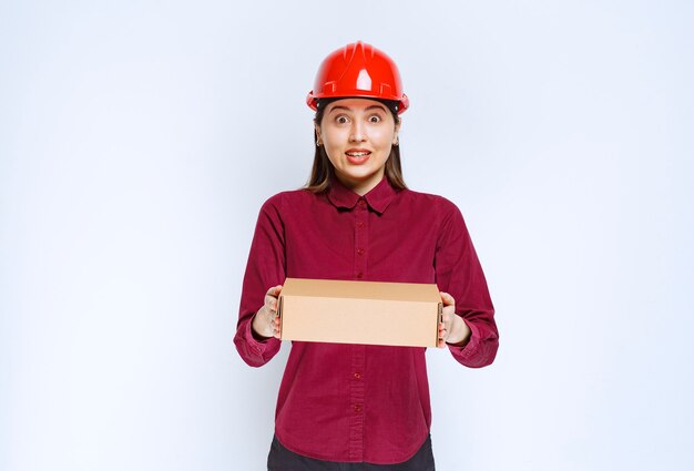 Foto van vrouw in rode helm met kartonnen doos op witte achtergrond.