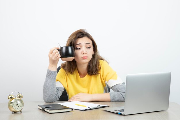 Foto van vrouwelijke kantoormedewerker die aan het bureau zit en een mok vasthoudt. Hoge kwaliteit foto