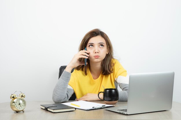 Foto van vrouwelijke kantoormedewerker zittend aan de balie en pratend op mobiele telefoon. hoge kwaliteit foto