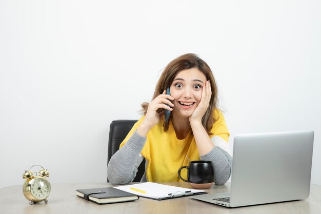 Foto van vrouwelijke kantoormedewerker zittend aan de balie en pratend op mobiele telefoon. Hoge kwaliteit foto