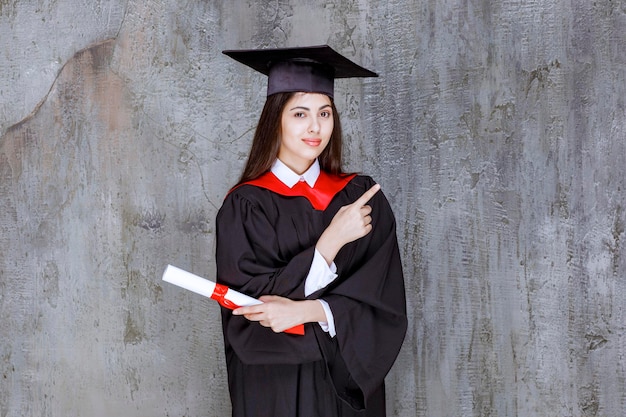 Gratis foto foto van vrouwelijke student die een toga draagt die ergens naar wijst. hoge kwaliteit foto