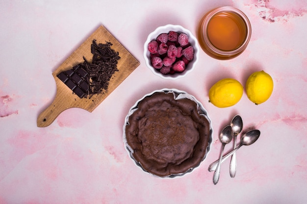 Framboos; citroen; olie; chocoladereep met vers bereide cake en lepels op roze gestructureerde achtergrond