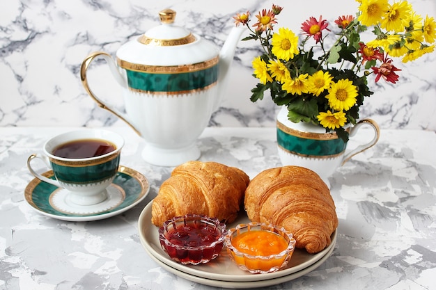 Frans ontbijt met croissants, abrikozenjam, kersenjam en een kopje thee, rode en gele bloemen